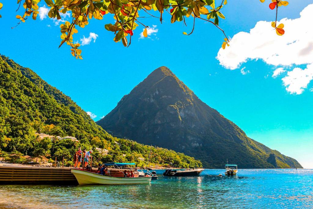 Boats moored at Jalousie Beach, with Gros Piton rising behind under a bright blue sky.